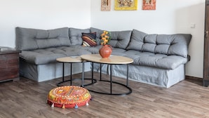 En moderne stue med en grå hjørnesofa, to runde sofaborde, en farverig skammel og en vase med blomster.
