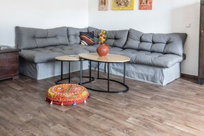 Ein modernes Wohnzimmer mit einem grauen Ecksofa, zwei runden Couchtischen, einem farbenfrohen Hocker und einer Blumenvase.