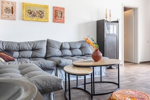 Un salon moderne avec un canapé d’angle gris, une petite table ronde en bois et un vase rempli de fleurs.