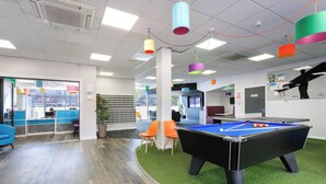 A modern indoor space with a pool table, bright overhead lighting, and a seating area with orange chairs.