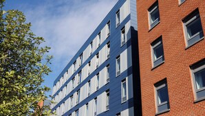 A multi-story building with a mix of brick and blue siding, featuring numerous windows and a clear sky.