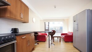 A modern kitchen with wooden cabinets, a stainless steel refrigerator, and a dining area with red chairs and a table.