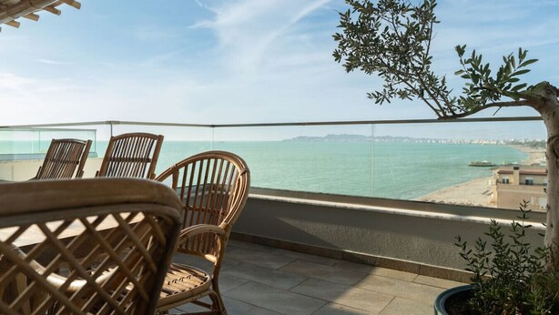 Un balcone con sedie in vimini, una pianta in vaso e vista sul mare e sulla costa in lontananza.