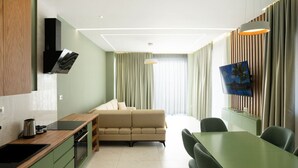Una moderna camera d'hotel con angolo cottura, divano, zona pranzo e TV a parete.