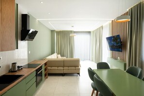 A modern hotel room with a kitchenette, a sofa, a dining area, and a TV mounted on the wall. - Penthouse Royal Orchid (Durrës)
