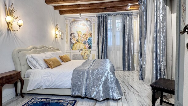 Ein Schlafzimmer mit Bett, Nachttisch, Wandleuchte und Wandgemälde.
