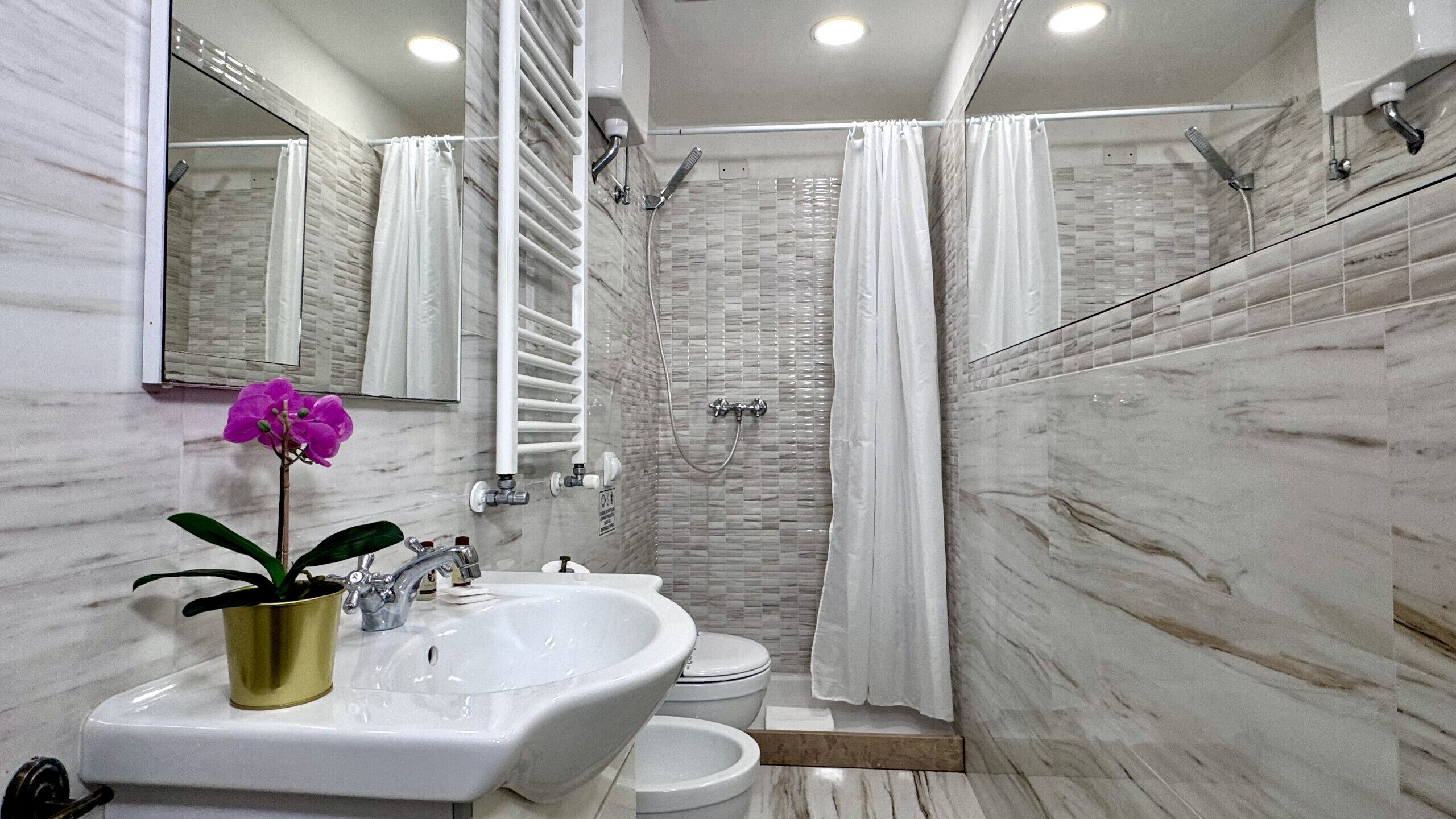 A bathroom with a marble wall, a shower, a sink, and a toilet.
