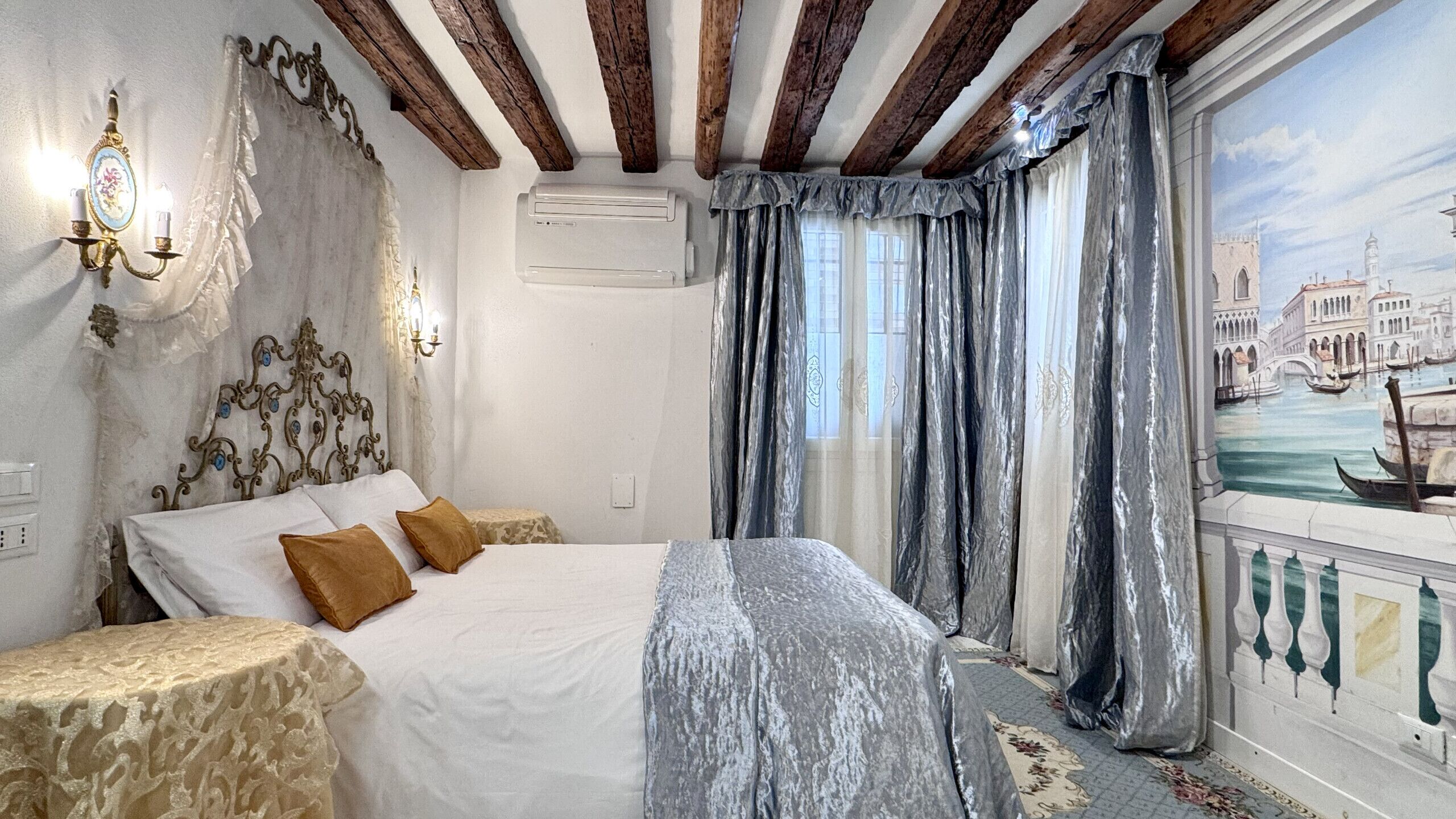 A bedroom with a bed, curtains, a wall-mounted air conditioner, and a window with a view of a canal.