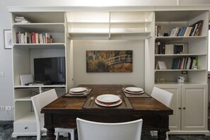 Un coin repas avec une table en bois dressée pour quatre personnes, entourée de chaises blanches, et des étagères de chaque côté.