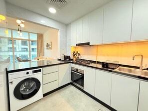 Eine moderne Küche mit weißen Schränken, einer integrierten Waschmaschine und einem großen Fenster mit Blick auf einen Balkon.
