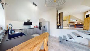 Eine moderne Küche mit Einbauofen, Mikrowelle und Kühlschrank. Ein Holztisch und eine Treppe zu einem Wohnbereich sind ebenfalls vorhanden.