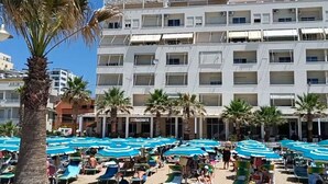 Um hotel com vários andares, áreas de estar ao ar livre com guarda-sóis azuis e palmeiras.