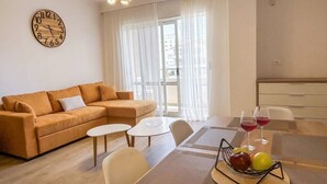 Uma sala de estar moderna com sofá, mesa de centro e mesa de jantar. Há um relógio na parede e uma janela com cortinas.