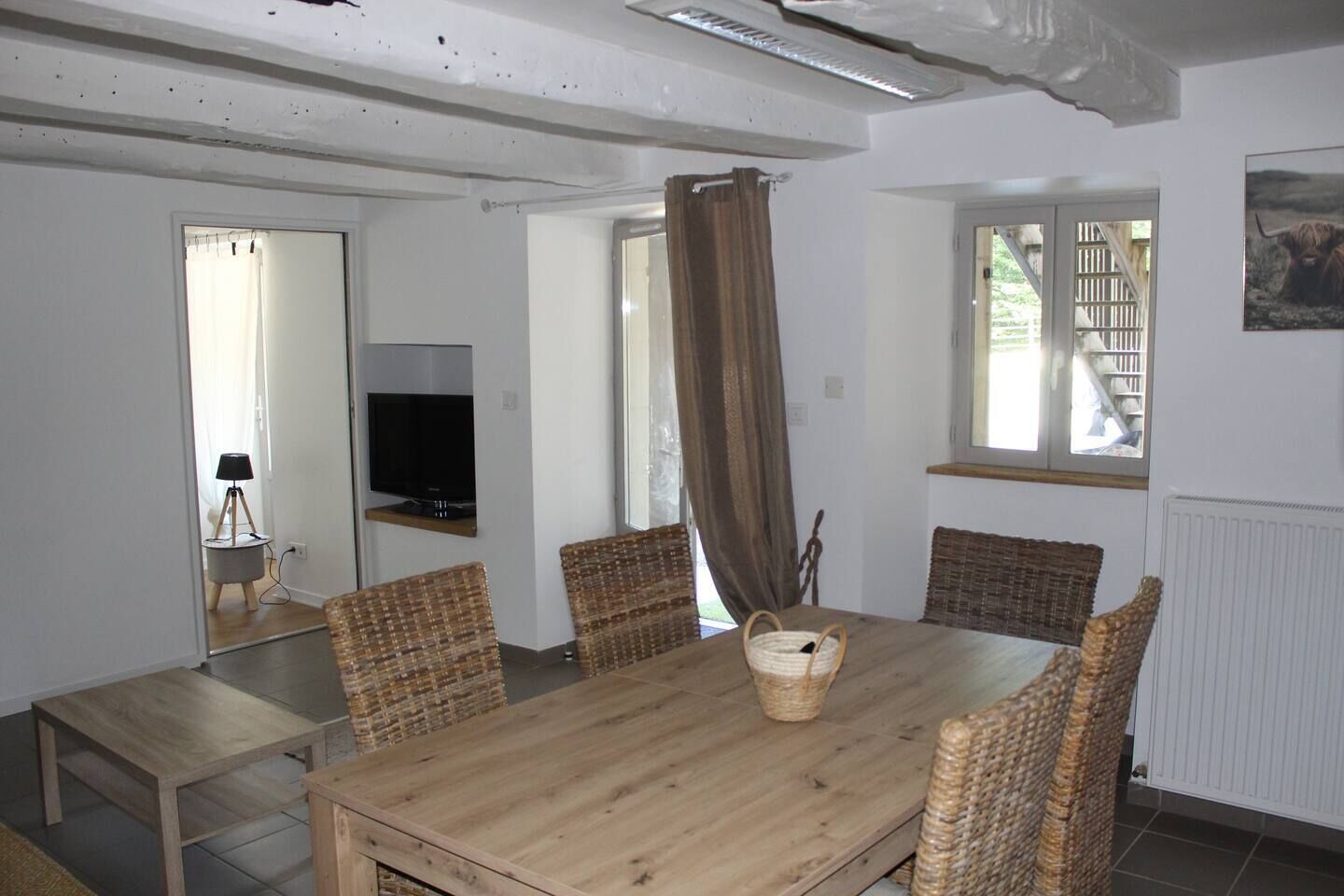 Ein Essbereich mit Holztisch, Korbstühlen, einem Fernseher auf einem Schrank und einem Fenster mit Vorhängen.