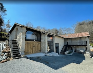 Ein zweistöckiges Steinhaus mit einer Holztreppe, die zu einem überdachten Eingang führt.
