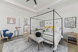 Une chambre à coucher moderne avec un lit à baldaquin, un banc, une table d’appoint et des œuvres d’art accrochées aux murs.