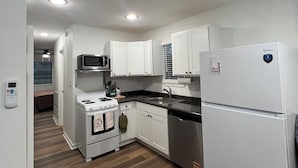 Una cocina pequeña con armarios blancos, microondas, estufa, fregadero y refrigerador.