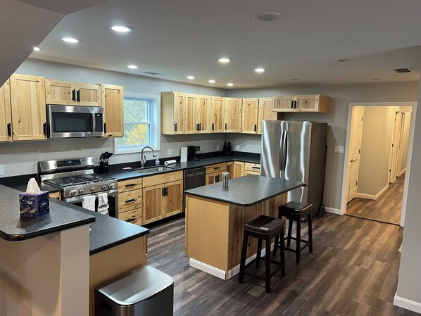 A modern kitchen with wooden cabinets, stainless steel appliances, and a central island with stools.