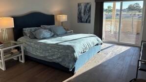 Un dormitorio con una cama grande, dos mesitas de noche, una mesilla auxiliar, una ventana con vistas y un ventilador de techo.