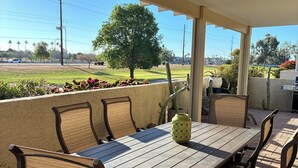 Un patio al aire libre con una mesa, sillas, un cactus y vistas a un campo con árboles.