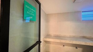 Una camera d'albergo con una porta in vetro, un cartello che indica 'Máquinas Lavas Roupas' e una piccola finestra con persiane.