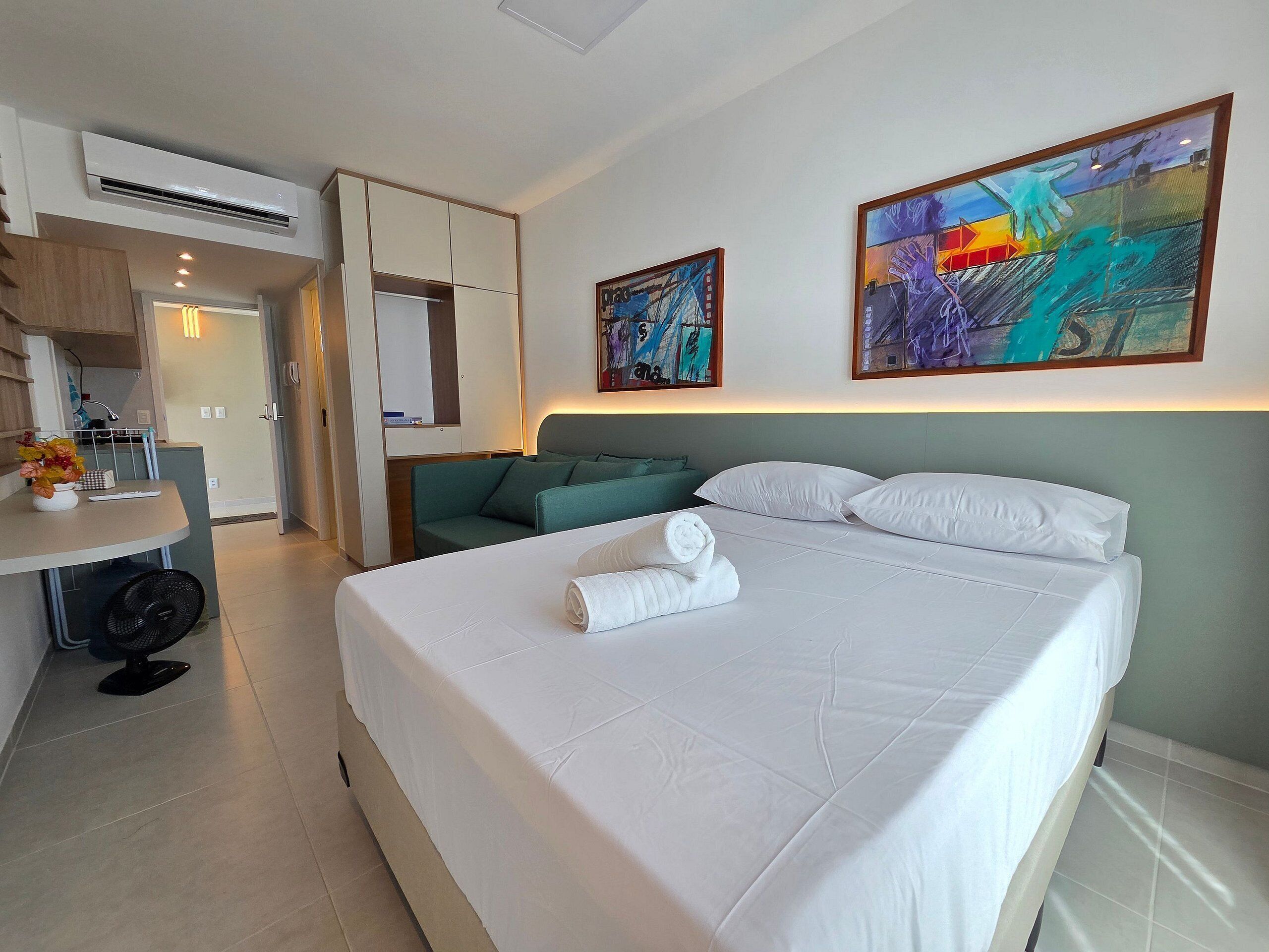 A hotel room with a bed, a desk, a chair, a sofa, and two paintings on the wall.