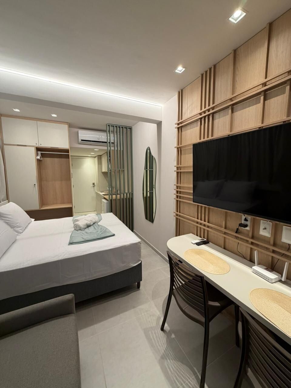 A modern hotel room with a bed, a desk, a flat-screen TV, and built-in shelving.