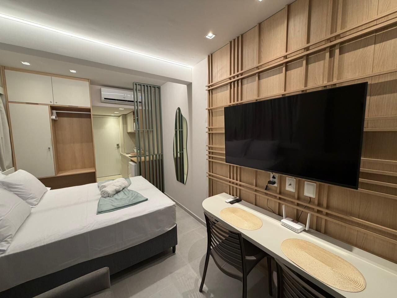 A modern hotel room with a bed, a desk, a flat-screen TV, and built-in wooden paneling.