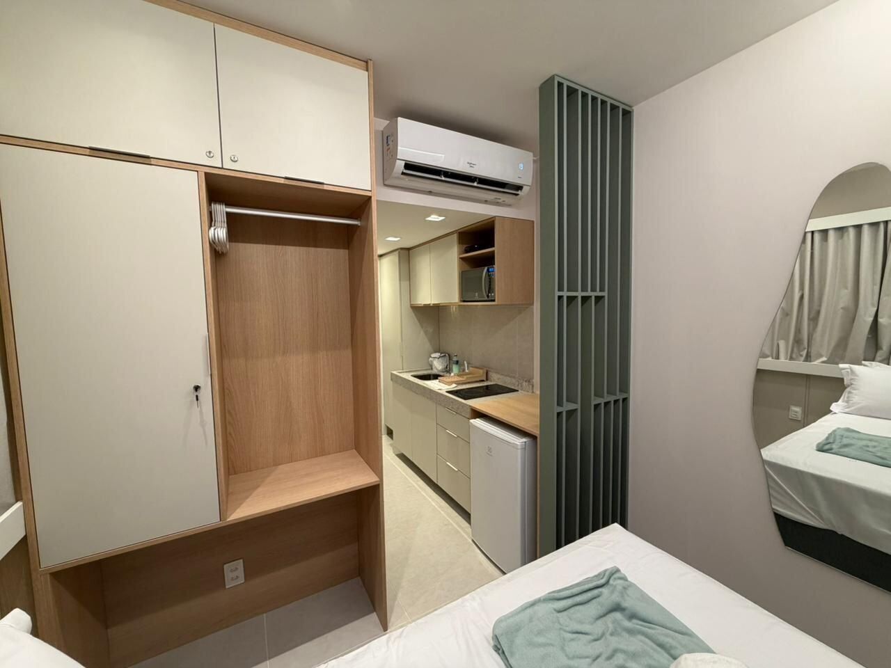 A compact bedroom with a bed, a wardrobe, a kitchenette, and an air conditioning unit.