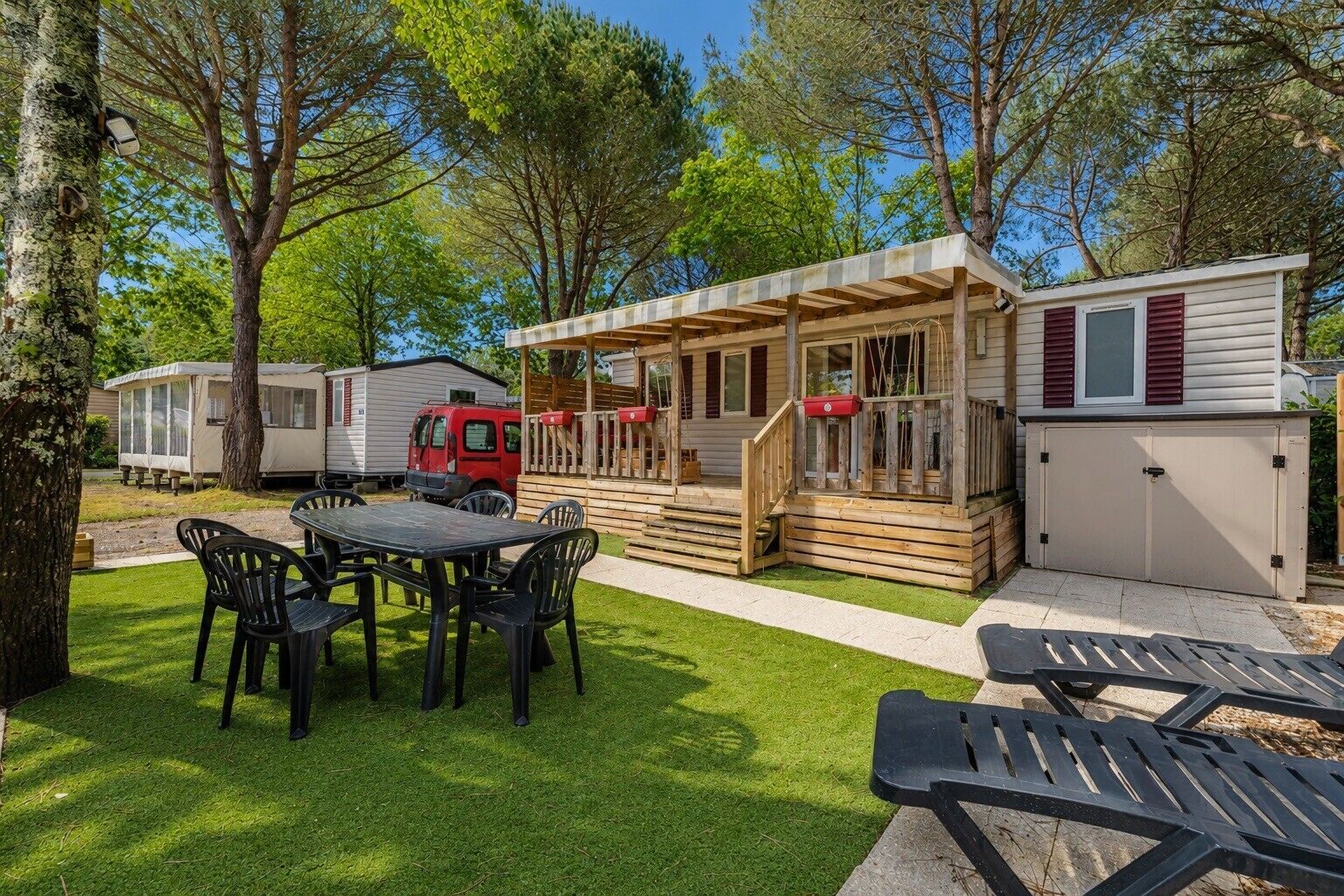Un camping con terraza de madera, mesa de picnic y vehículos recreativos.