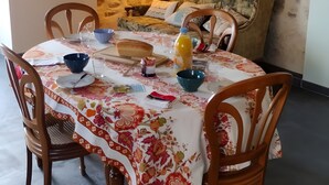 Une table à manger recouverte d’une nappe à motifs floraux, des chaises en bois, un mur en pierre, un canapé et une lampe suspendue.