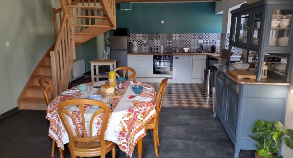 A dining area with a table set for four, a staircase, and a kitchen with patterned backsplash and cabinets. - Holiday Home 'La Maison De Béatrice' with Mountain View, Private Terrace and Wi-Fi (Oberbruck)