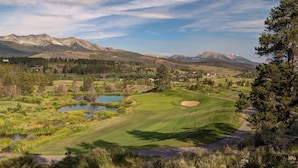 Ein Golfplatz mit Teich, umgeben von Bergen und Bäumen.