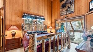 Ein Schlafzimmer einer Holzhütte mit Bett, zwei Nachttischlampen, einem Holzvorhang und einem Fenster mit Aussicht sowie einer Tür.