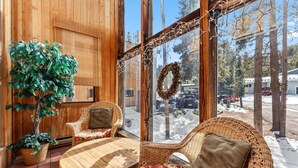 Ein gemütliches Zimmer mit Holzvertäfelung, Korbmöbeln, einem Blumentopf und Blick auf eine verschneite Landschaft.