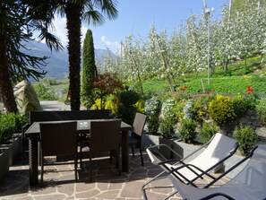 An outdoor seating area with a table and chairs, surrounded by lush greenery and flowering plants. - Apartment 'Gartenrose' with Mountain View, Shared Pool and Wi-Fi (Naturno)
