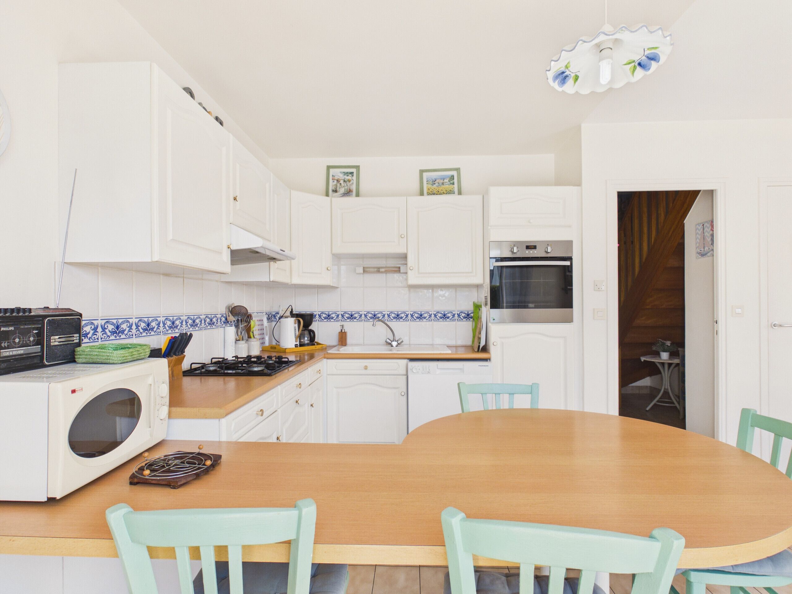 Una cocina compacta con armarios blancos, una mesa de comedor de madera y sillas color turquesa.