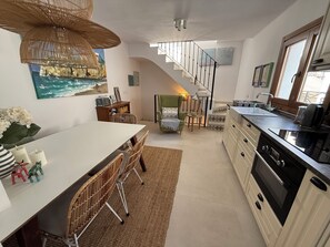 A modern kitchen with a central island, a dining area with wicker chairs, a staircase, and a view of the ocean through a window. - Casa Las Brisas - Rooftop Terrace & Sea View - Mediterranean cozy Townhouse (Algarrobo-Costa)