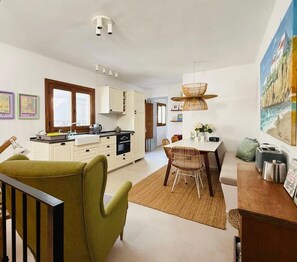 A modern kitchen with white cabinets, a dining area with a table and chairs, and a large painting on the wall. - Casa Las Brisas - Rooftop Terrace & Sea View - Mediterranean cozy Townhouse (Algarrobo-Costa)