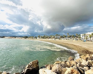 A beach with clear water, rocky shoreline, and a row of palm trees and buildings along the shore. - Casa Las Brisas - Rooftop Terrace & Sea View - Mediterranean cozy Townhouse (Algarrobo-Costa)