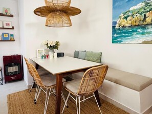 A dining area with a white table, wicker chairs, a bench, a woven pendant light, a wall-mounted painting, and a red heater. - Casa Las Brisas - Rooftop Terrace & Sea View - Mediterranean cozy Townhouse (Algarrobo-Costa)