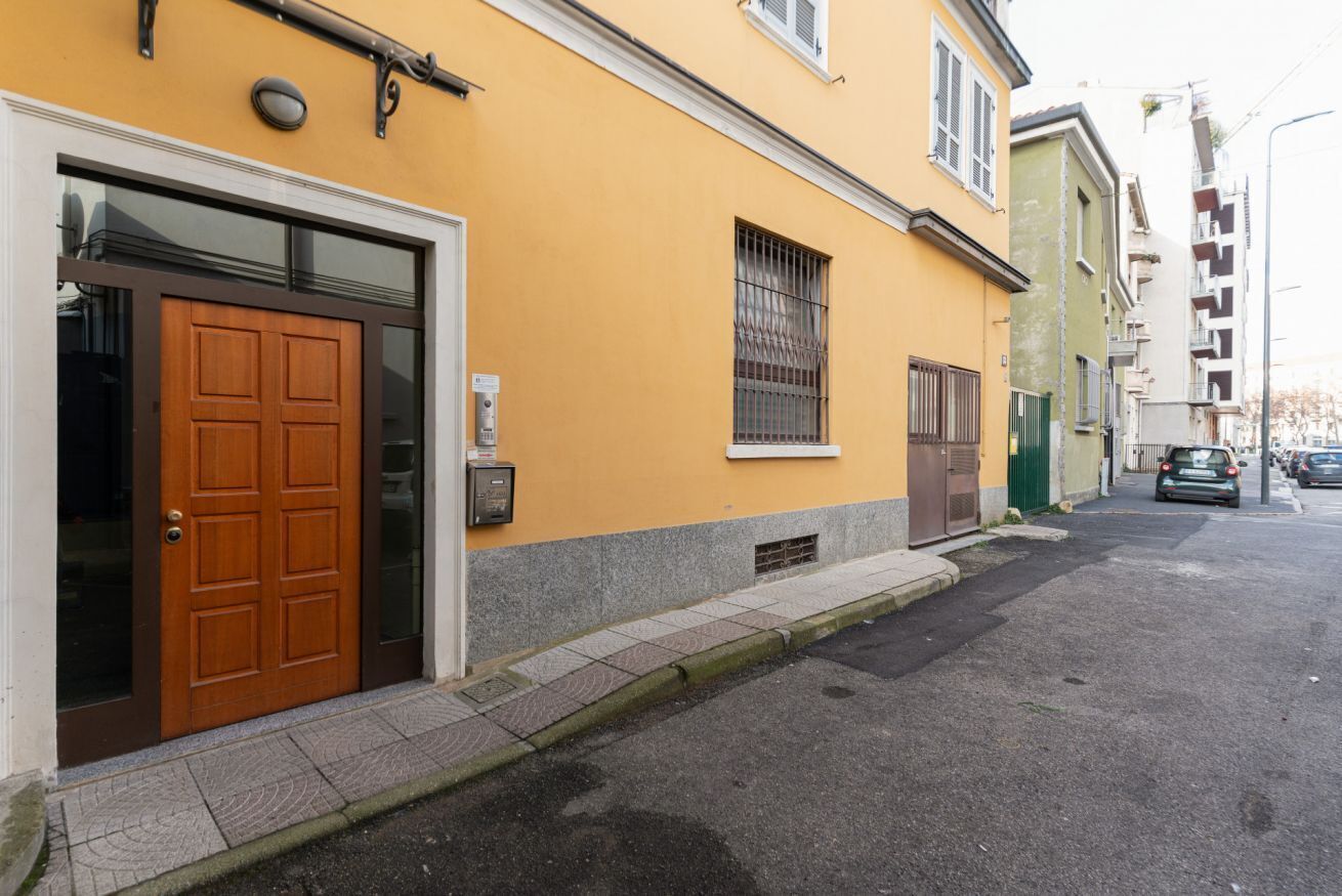 En gul byggnad med en trädörr, ett fönster med galler och ett litet markis.