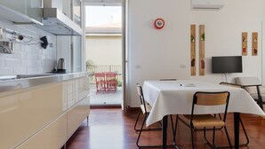 A kitchen with a dining area, a TV, and a balcony with red chairs. - GuestHost - Cozy 50m2 apartment, perfect for 2 people, located on the first floor of a building with lift.The accommodation is located in the Derganino area, about 600 meters from the Lancetti railway station and just over 1 km from the Maciachini  (Milan)