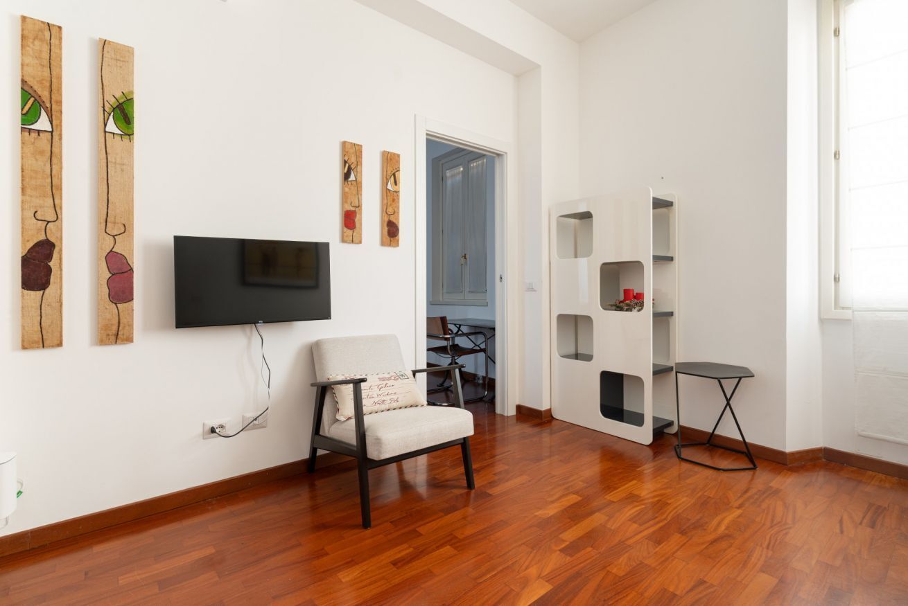 Une pièce avec un plancher en bois, une chaise, un téléviseur fixé au mur et une bibliothèque.