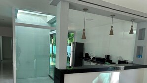A modern kitchen with a black countertop, white cabinets, and pendant lights. - Casa Parque das Árvores - Camaçari - BA (Camaçari)