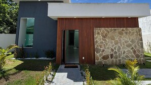 A modern two-story house with a stone facade and a wooden door. - Casa Parque das Árvores - Camaçari - BA (Camaçari)