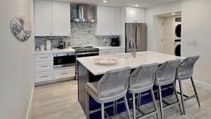 Una cocina moderna con armarios blancos, una isla grande con taburetes de bar, un refrigerador de acero inoxidable y un horno empotrado.