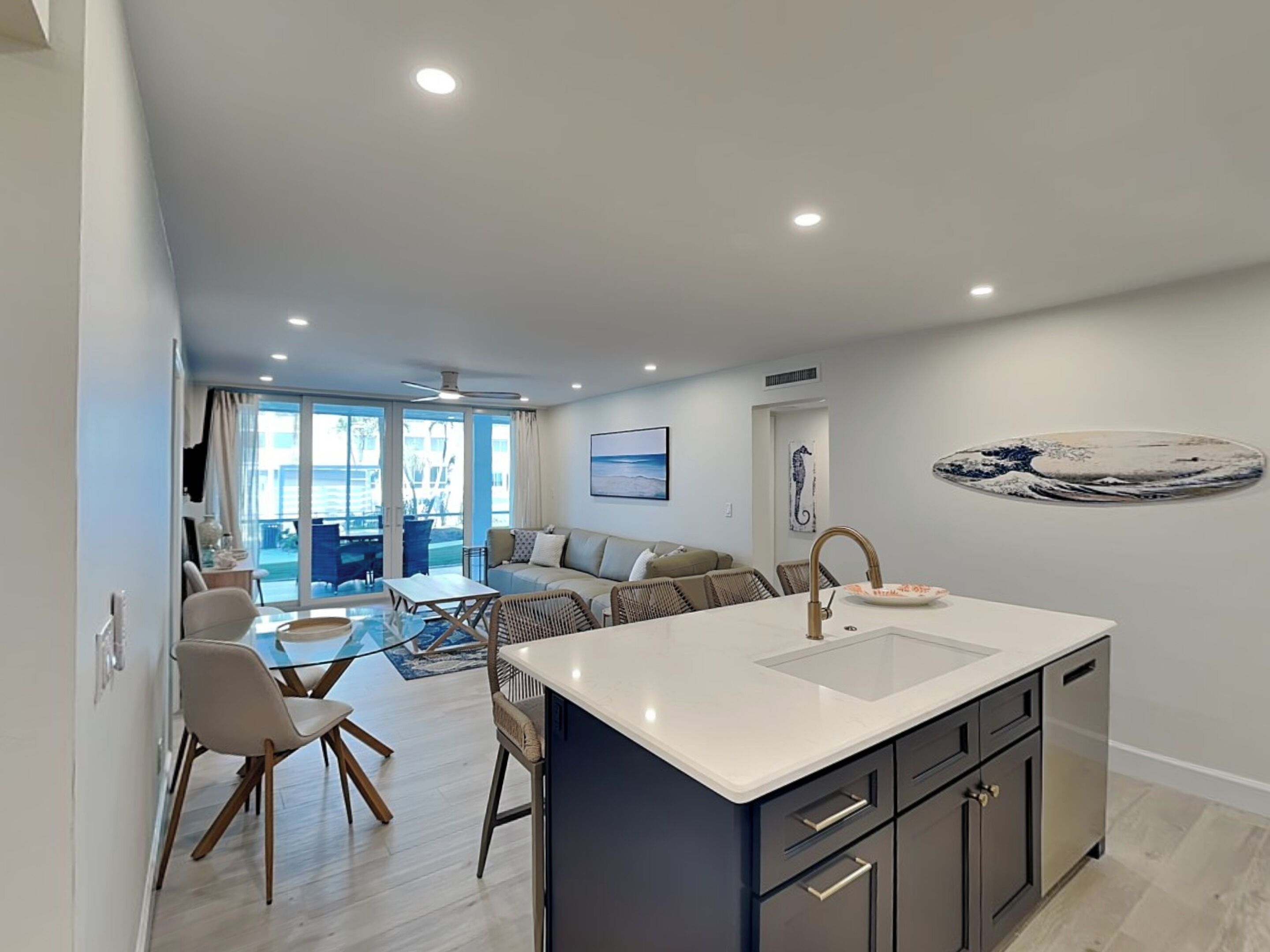 A modern kitchen with a central island, dining area with chairs, and a living room with a sofa and chairs.