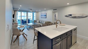 Una cocina moderna con una isla central, comedor con sillas y sala de estar con sofá y sillones.