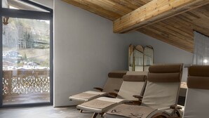 Een spa-ruimte met houten balken in het plafond, grote ramen en drie ligstoelen met handdoeken.